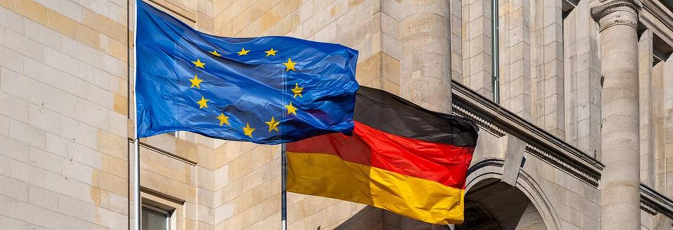 In Großaufnahme wehen vor einem Gebäude die deutsche und die europäische Flagge.