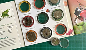 Ins geöffnete Sammelalbum „Wunderwelt Insekten“ sind einige Münzen der Serie eingeklickt.