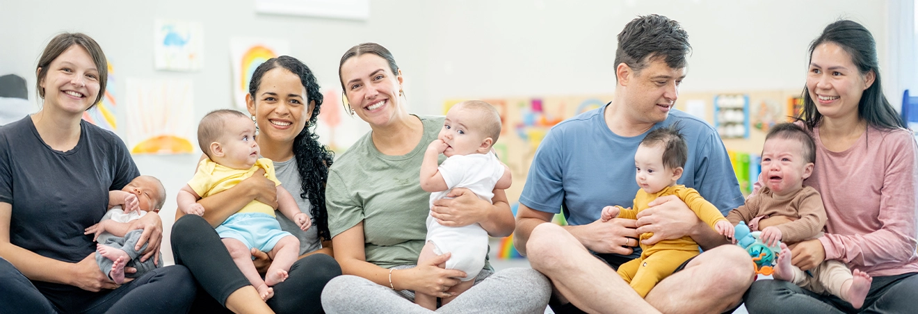 Mütter und Väter sitzen mit ihren Babys auf dem Schoß in einem Übungsraum.