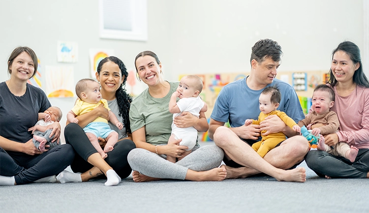 Mütter und Väter sitzen mit ihren Babys auf dem Schoß in einem Übungsraum.