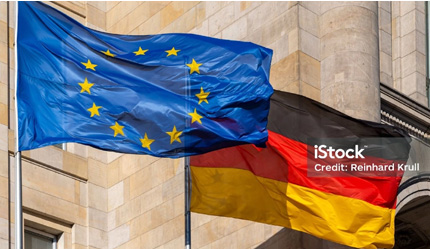In Großaufnahme wehen vor einem Gebäude die deutsche und die europäische Flagge.
