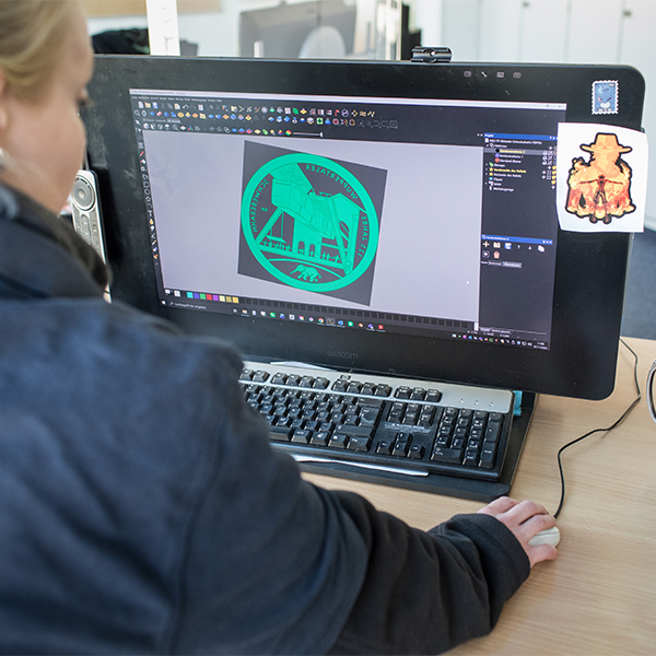 Eine Graveurin betrachtet den Entwurf der Silbermünze „125 Jahre Wuppertaler Schwebebahn“ auf dem Bildschirm.